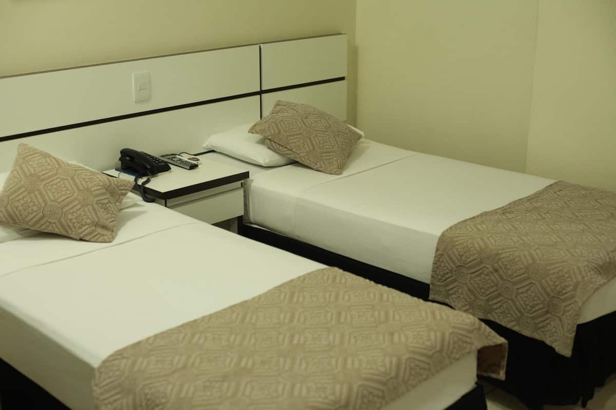 A hotel room with two single beds, each with patterned bedding and a bedside table with a phone and charger.