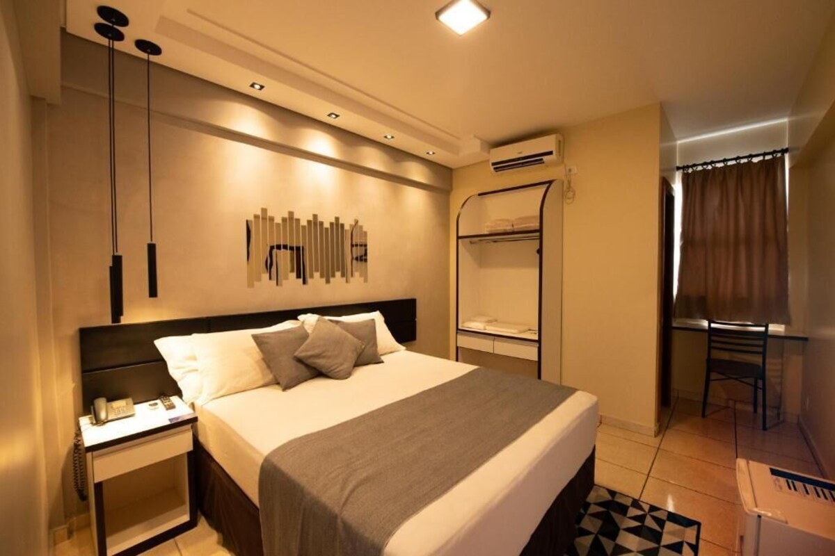 A hotel room with a bed, bedside table, wall art, a desk, and a chair.