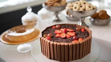 Uma mesa de sobremesas com um bolo de chocolate coberto com morangos e raspas de chocolate, rodeada por diversos doces assados.