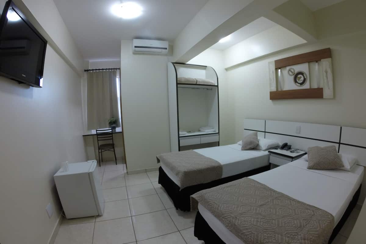 A hotel room with two beds, a desk, a mirror, an air conditioner, and a TV.