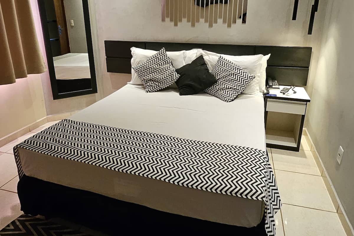 A modern bedroom with a large bed, a bedside table, a nightstand, a mirror, and an air conditioning unit.