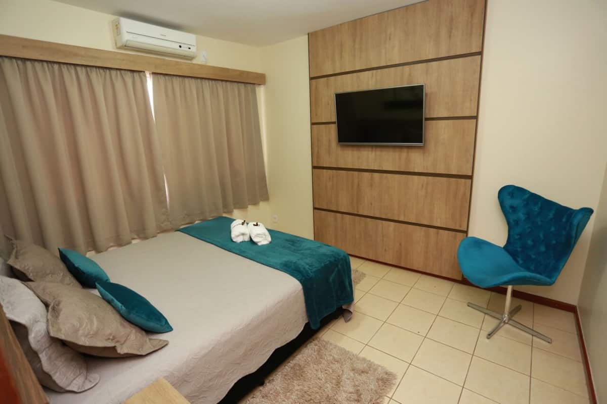 A bedroom with a bed, a TV mounted on the wall, and a chair.