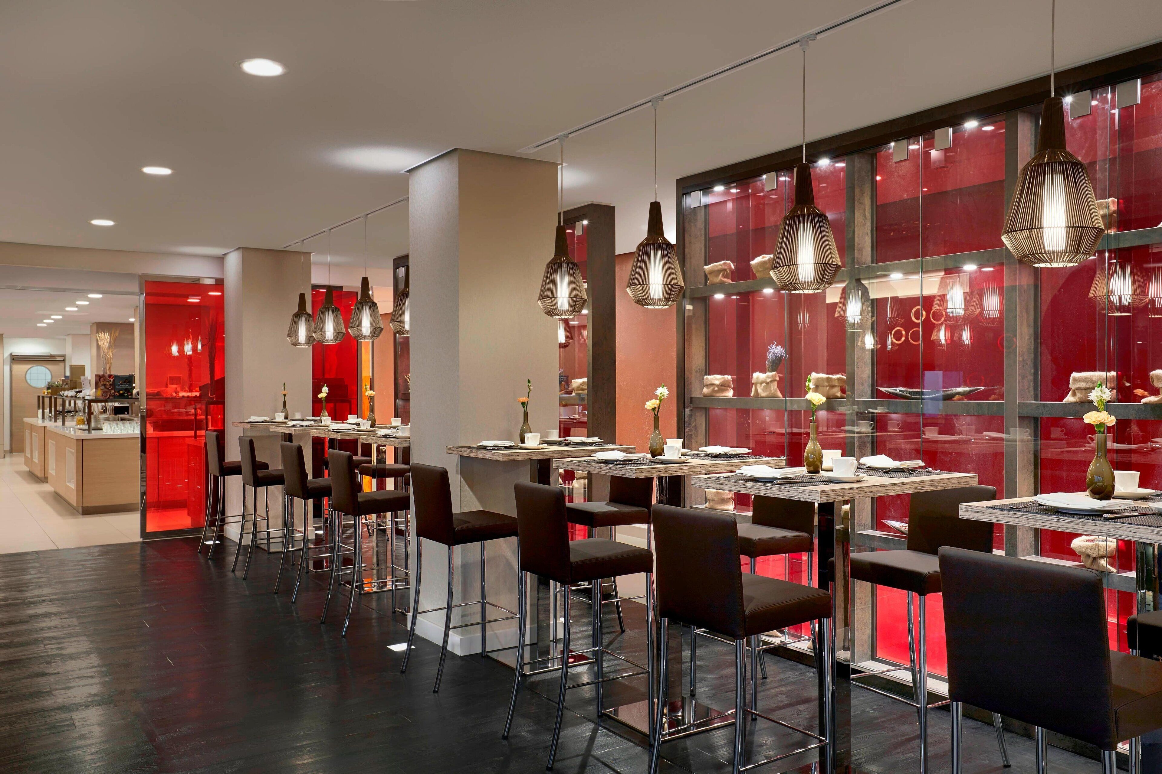 A modern restaurant with multiple tables and chairs, featuring pendant lighting and red accents.