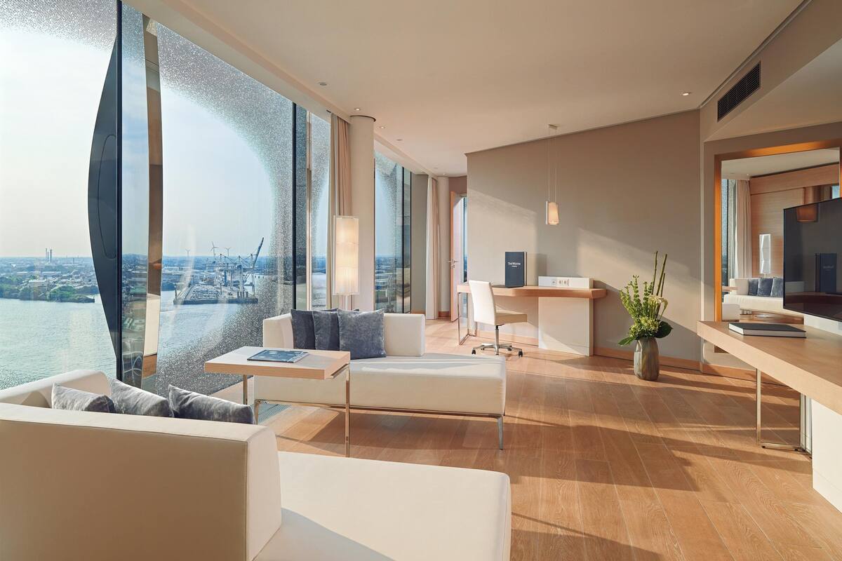 Une chambre d’hôtel moderne dotée d’une grande fenêtre donnant sur la ville, d’un coin salon confortable, d’un bureau et d’un décor minimaliste.