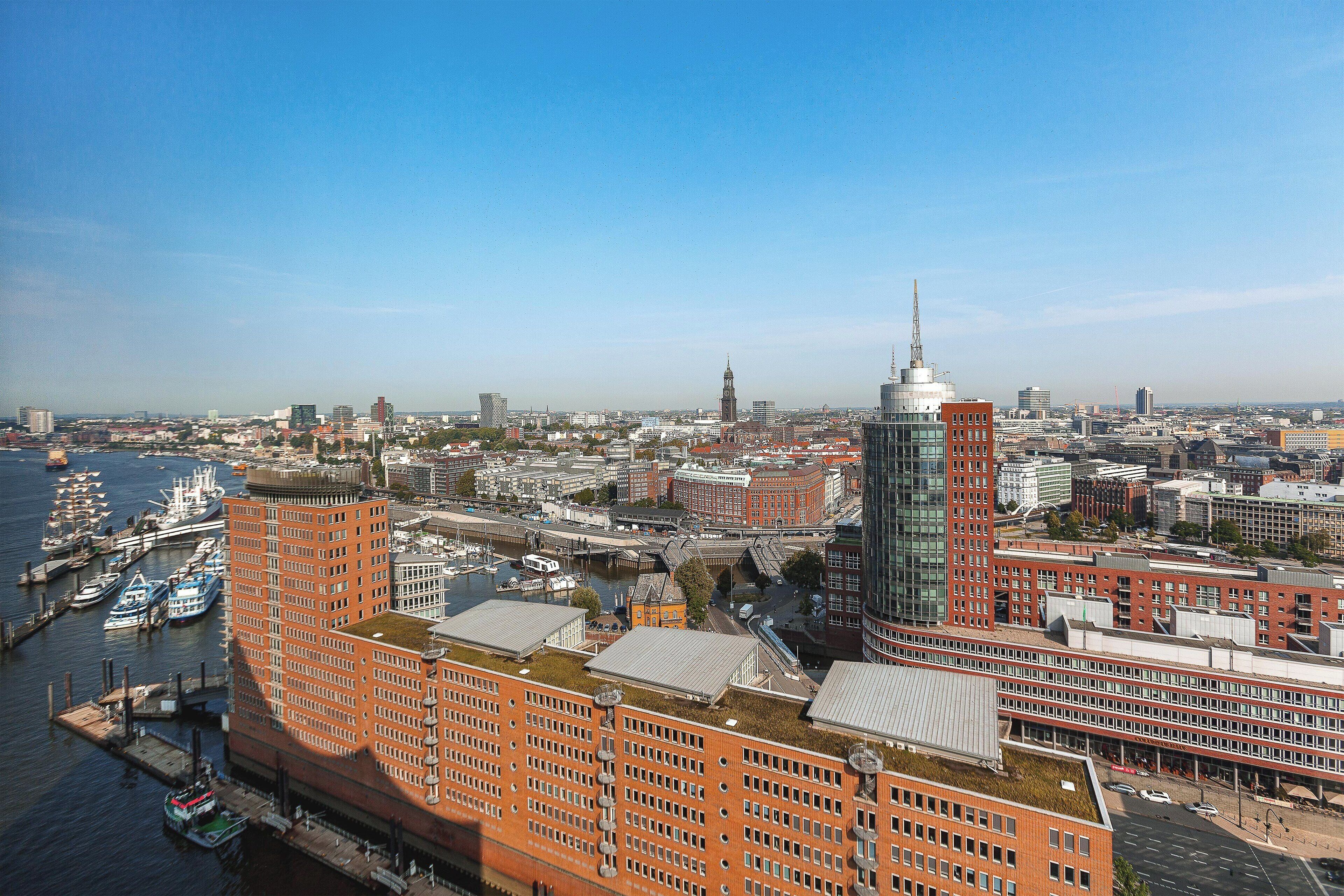 Ein Hochhaus mit moderner Glasfassade, ein Gebäude mit roten Ziegeln und einem grünen Dach, sowie ein Fluss mit Booten im Vordergrund.