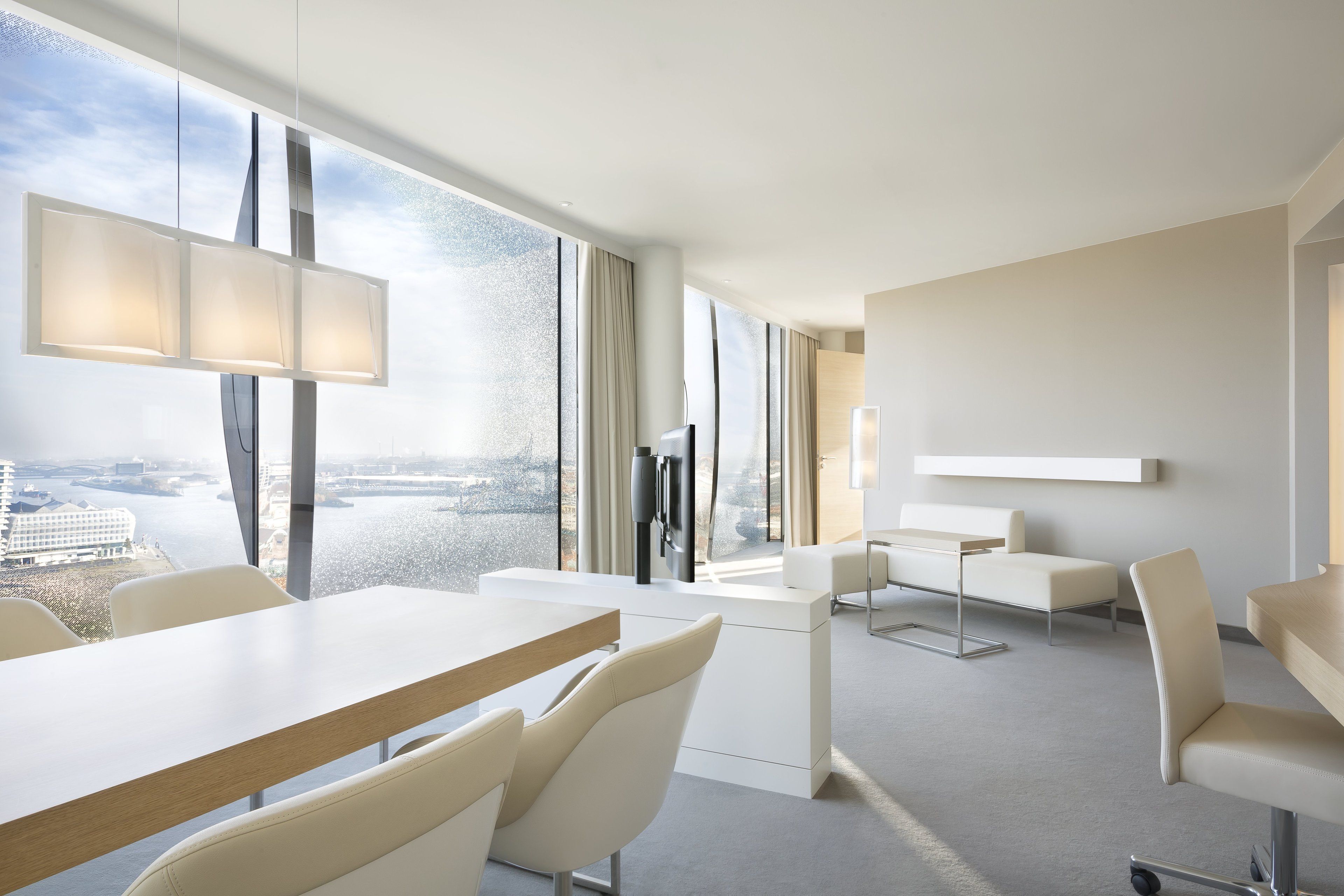 Ein modernes Hotelzimmer mit großem Fenster und Blick auf die Stadt, einem Flachbildfernseher, einem Schreibtisch und bequemen Sitzgelegenheiten.