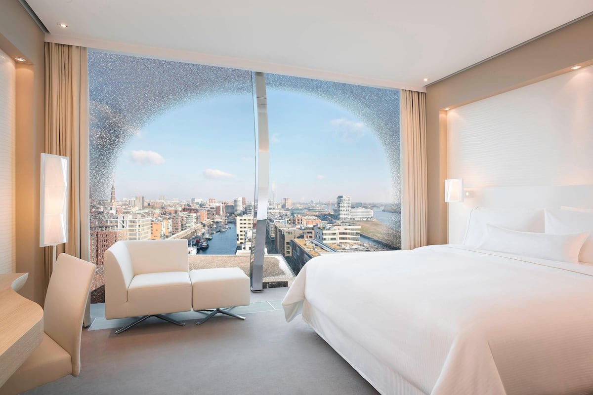 Une chambre d’hôtel moderne dotée d’une grande fenêtre donnant sur la ville, d’un lit, d’un coin salon et d’un bureau.