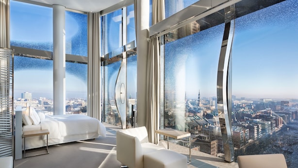 Ein modernes Hotelzimmer mit weitreichendem Stadtblick, einem Bett, einer Couch und einem kleinen Tisch.