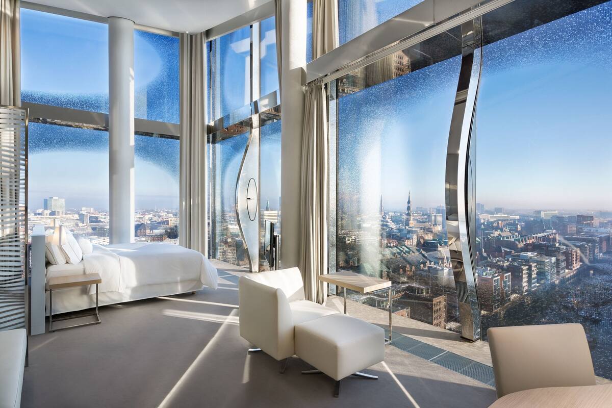 Une chambre d’hôtel moderne offrant une vue imprenable sur la ville, avec un lit, un canapé et une petite table.