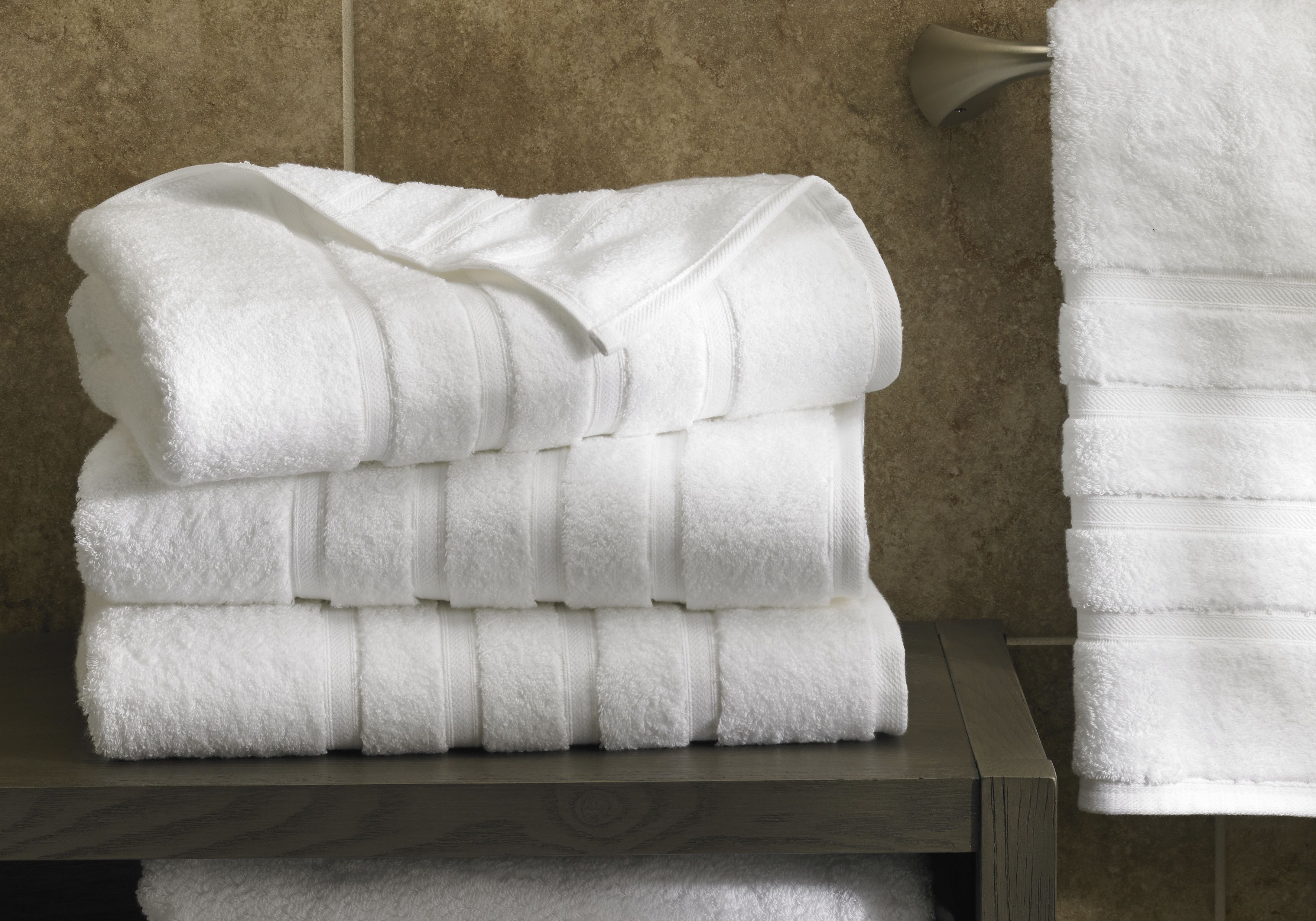 A stack of white towels on a wooden surface in a bathroom with a tiled wall.