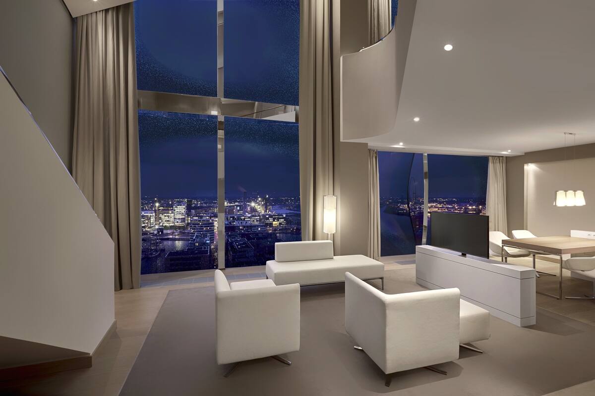 Une chambre d’hôtel moderne avec vue sur la ville, une grande fenêtre, un téléviseur à écran plat et un coin repas.