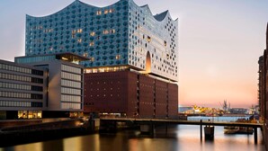 Ein modernes Hotel mit einer markanten, wellenförmigen Fassade, gelegen in der Nähe eines Uferbereichs mit einer Brücke.