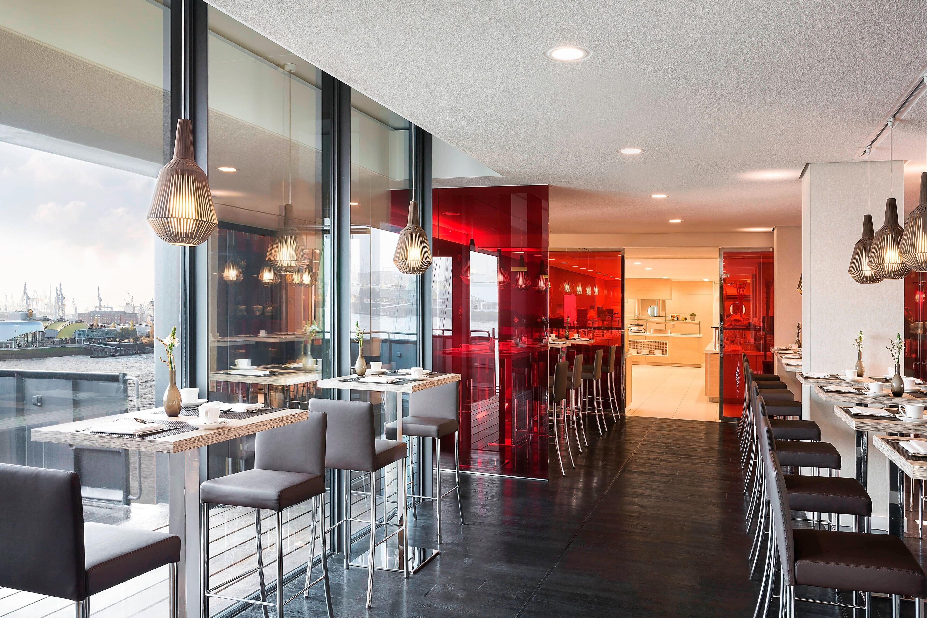 A modern restaurant with high tables and chairs, large windows, and a view of the city.