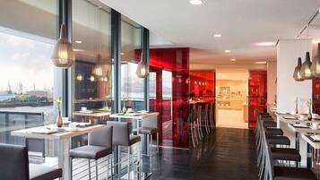 A modern restaurant with high tables and chairs, large windows, and a view of the city.