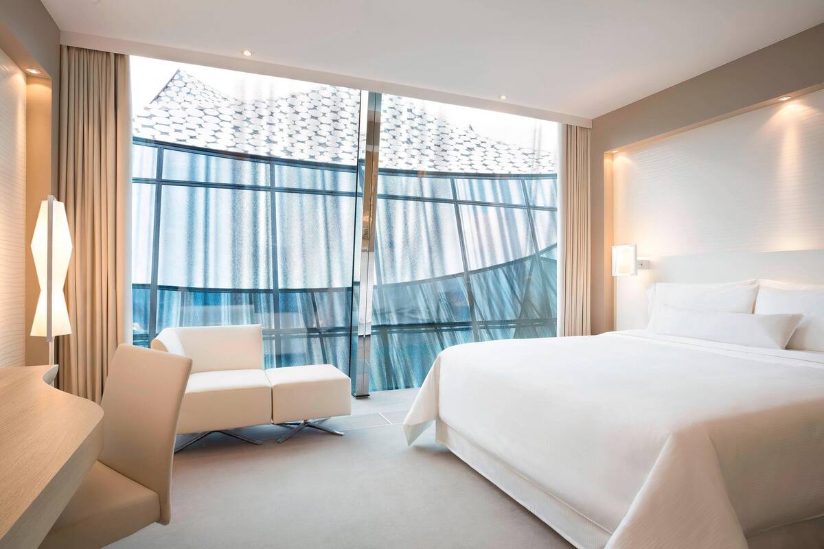 Une chambre d’hôtel moderne dotée d’un grand lit, d’un coin salon et offrant une vue sur l’extérieur grâce à une grande fenêtre.