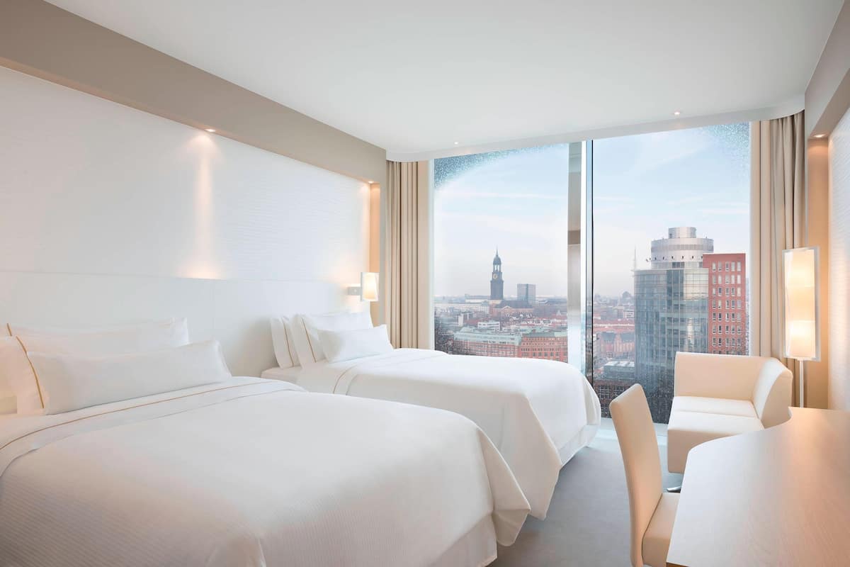 Une chambre d’hôtel avec deux lits, une table à manger et une vue sur le paysage urbain.