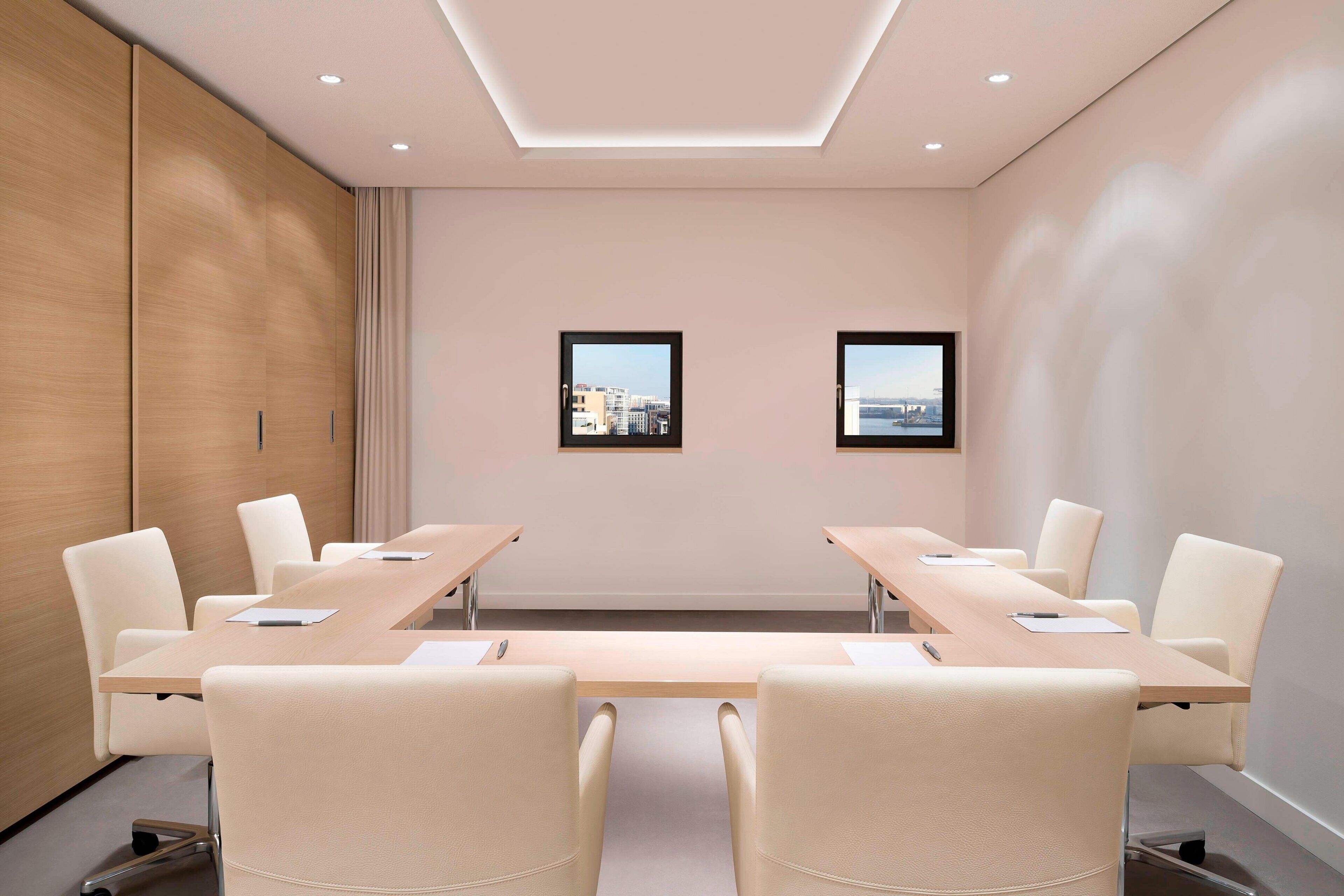 A conference room with a long table, six chairs, and two windows with city views.