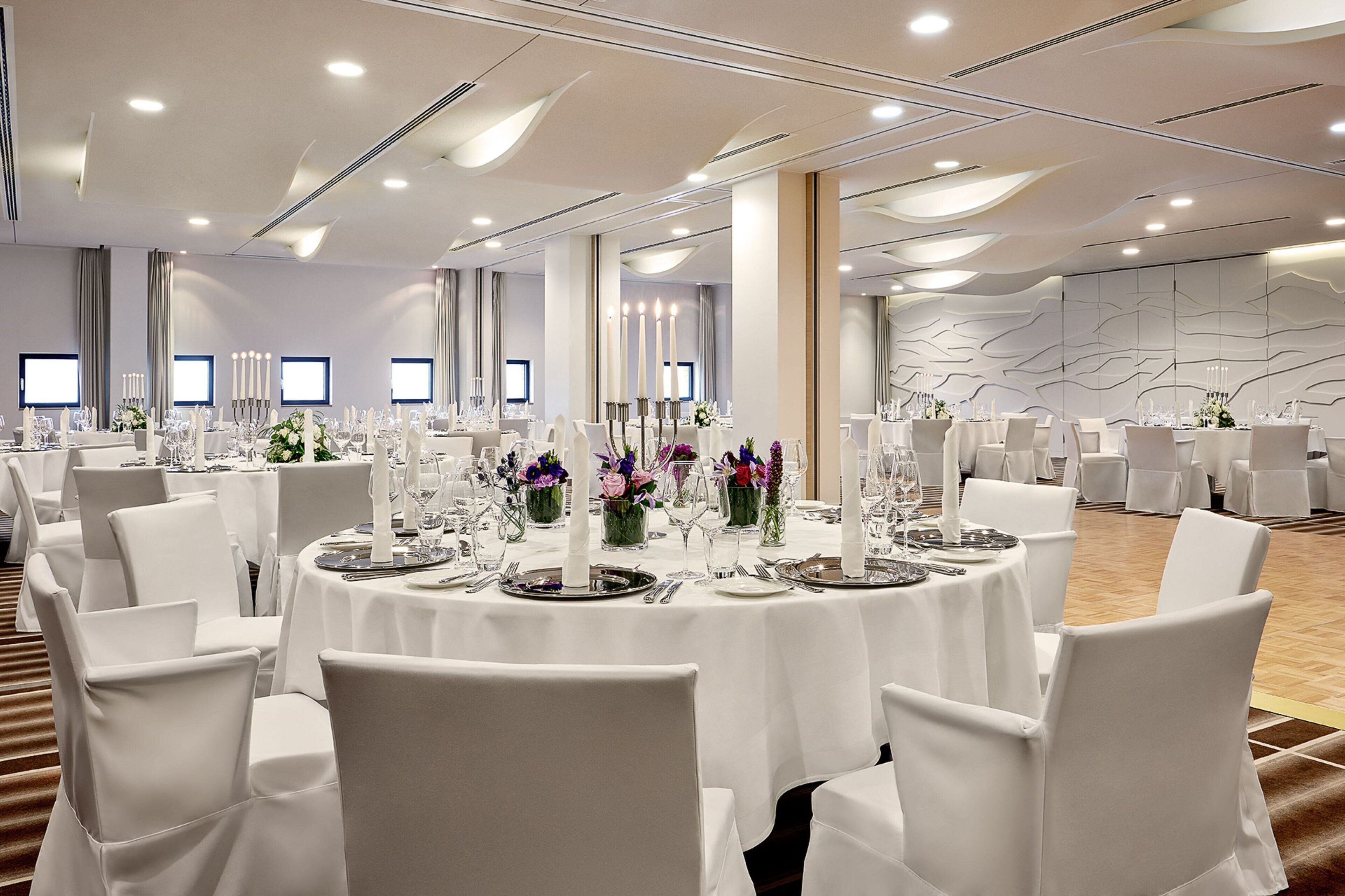 A banquet hall with round tables set for dining, white chairs, and floral centerpieces.