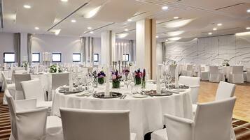 A banquet hall with round tables set for dining, white chairs, and floral centerpieces.