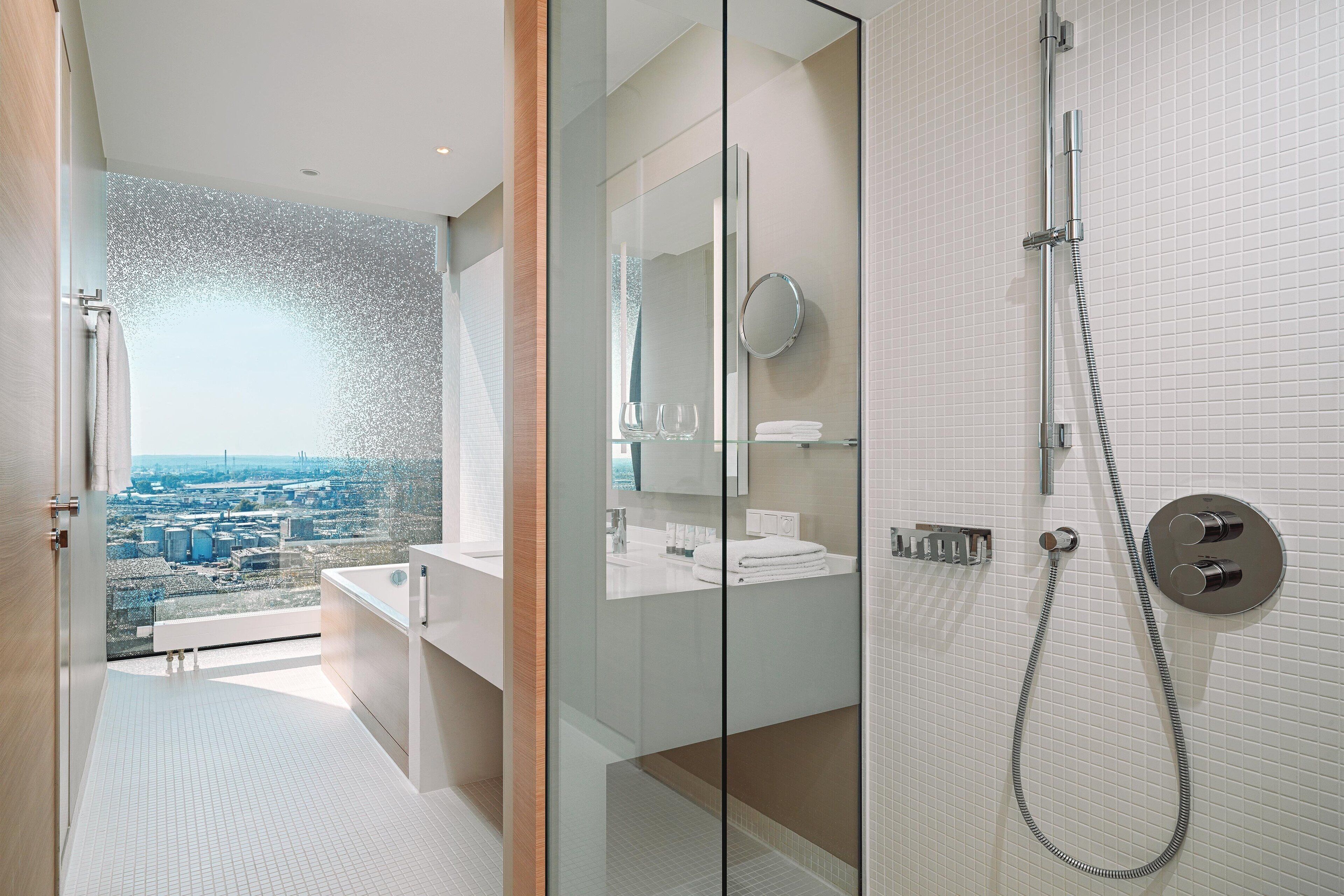 Ein modernes Badezimmer mit Duschkabine aus Glas, Blick auf die Stadt und einem großen Spiegel.