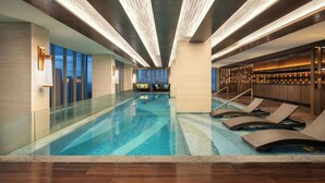 Una piscina interna moderna con acqua cristallina, poltrone relax e vista sulla città attraverso ampie finestre.