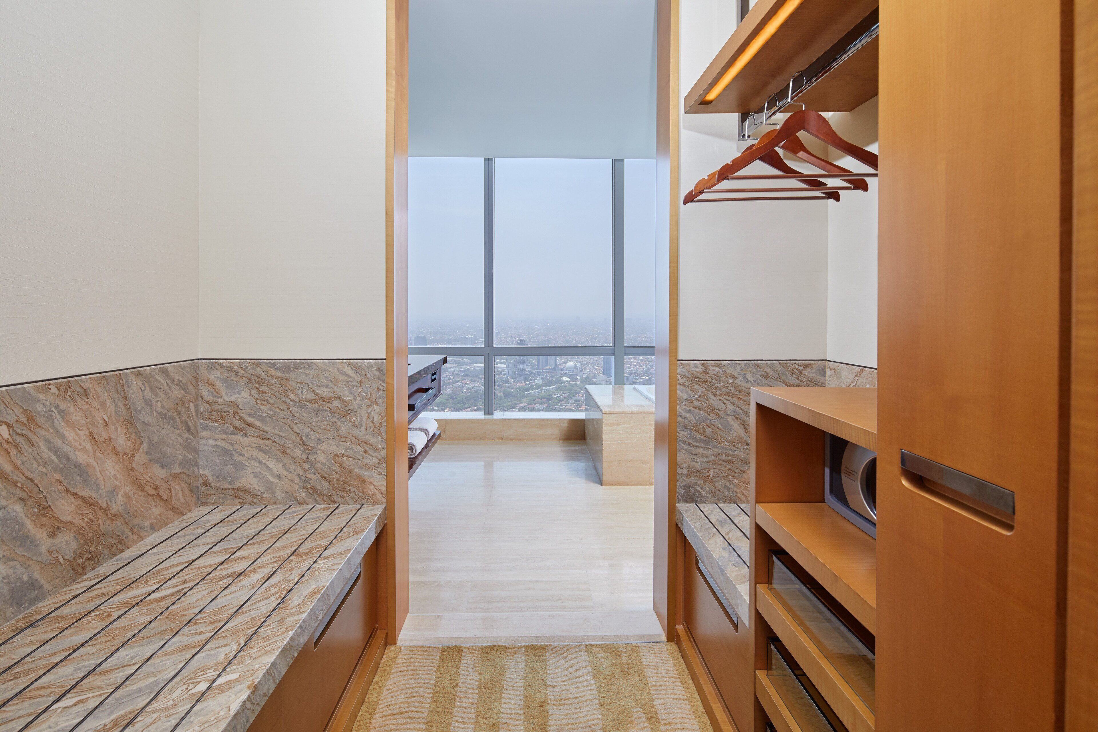 A modern bathroom with a marble floor, wooden vanity, and a view of the city through large windows.