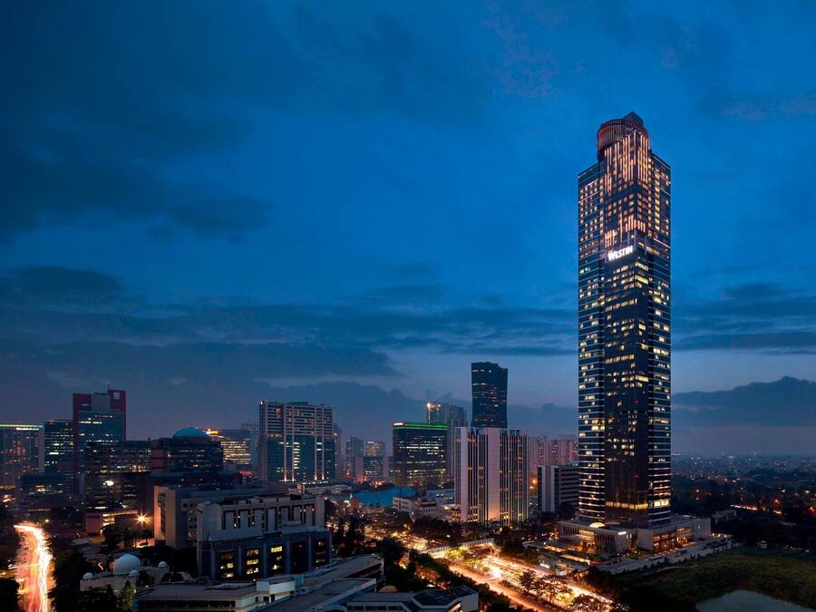 A high-rise building with a modern design, surrounded by other buildings and a busy street at dusk.