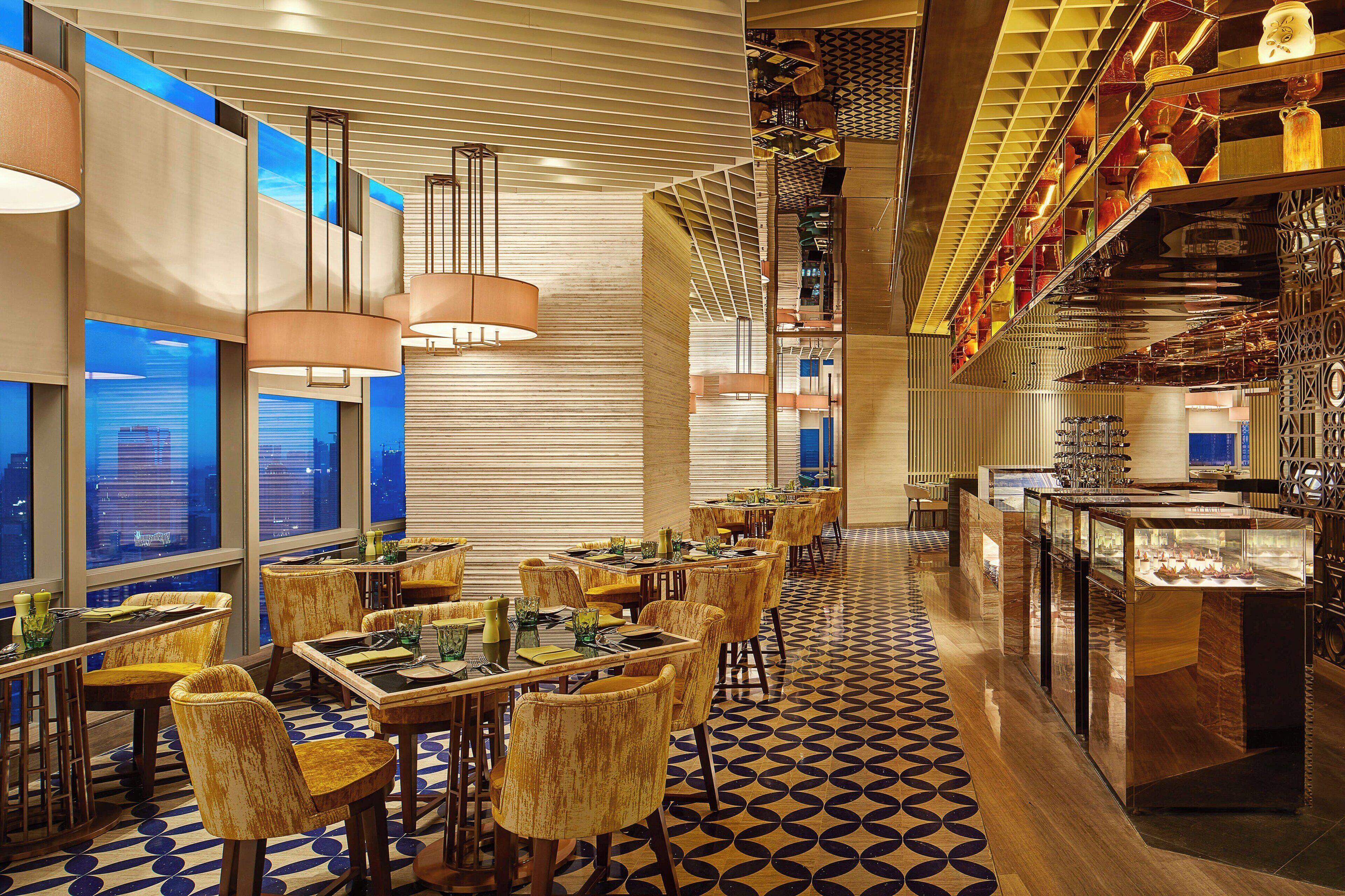 A modern restaurant with high tables and chairs, large windows, and a patterned floor.