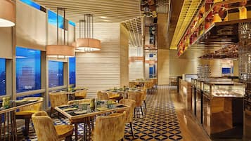 A modern restaurant with high tables and chairs, large windows, and a patterned floor.