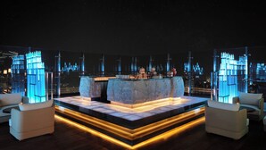 Zona bar moderna con bancone in marmo, posti a sedere e vista sulla città di notte.