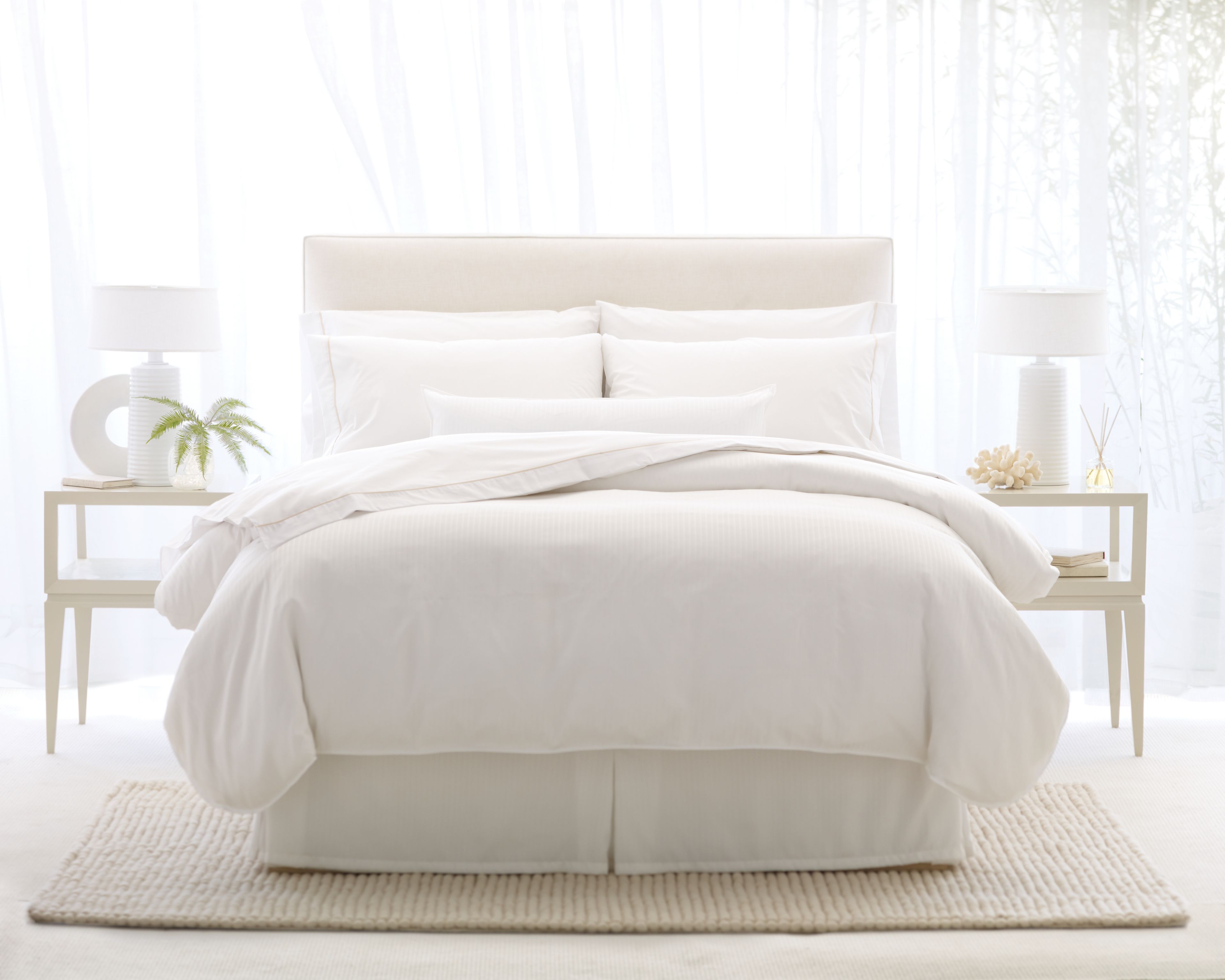 A neatly made bed with white bedding and pillows, flanked by two bedside tables with lamps and decorative items.