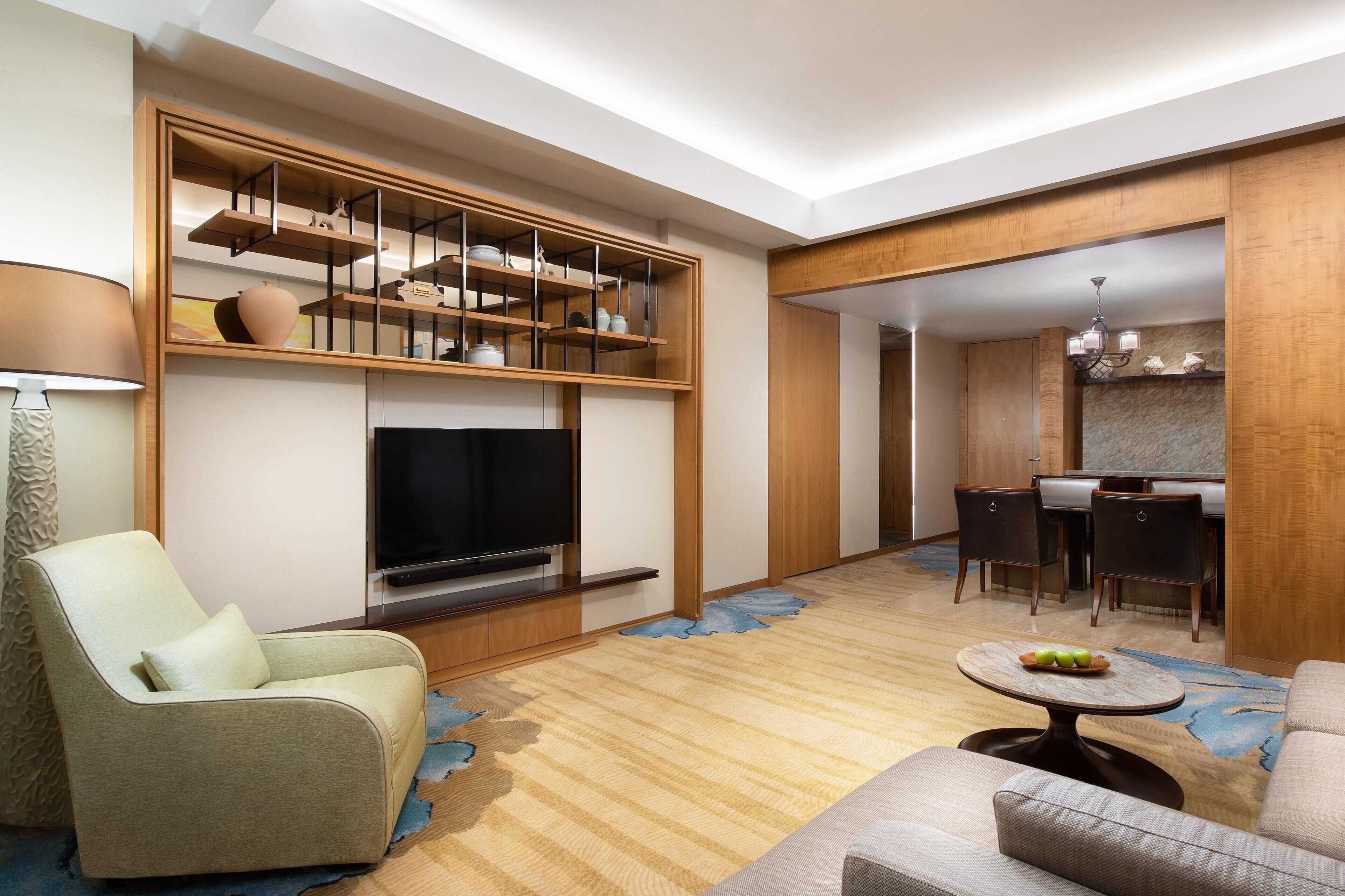Una sala moderna con un televisor de pantalla plana, un sofá, una zona de comedor con mesa y sillas, y una cocina al fondo.