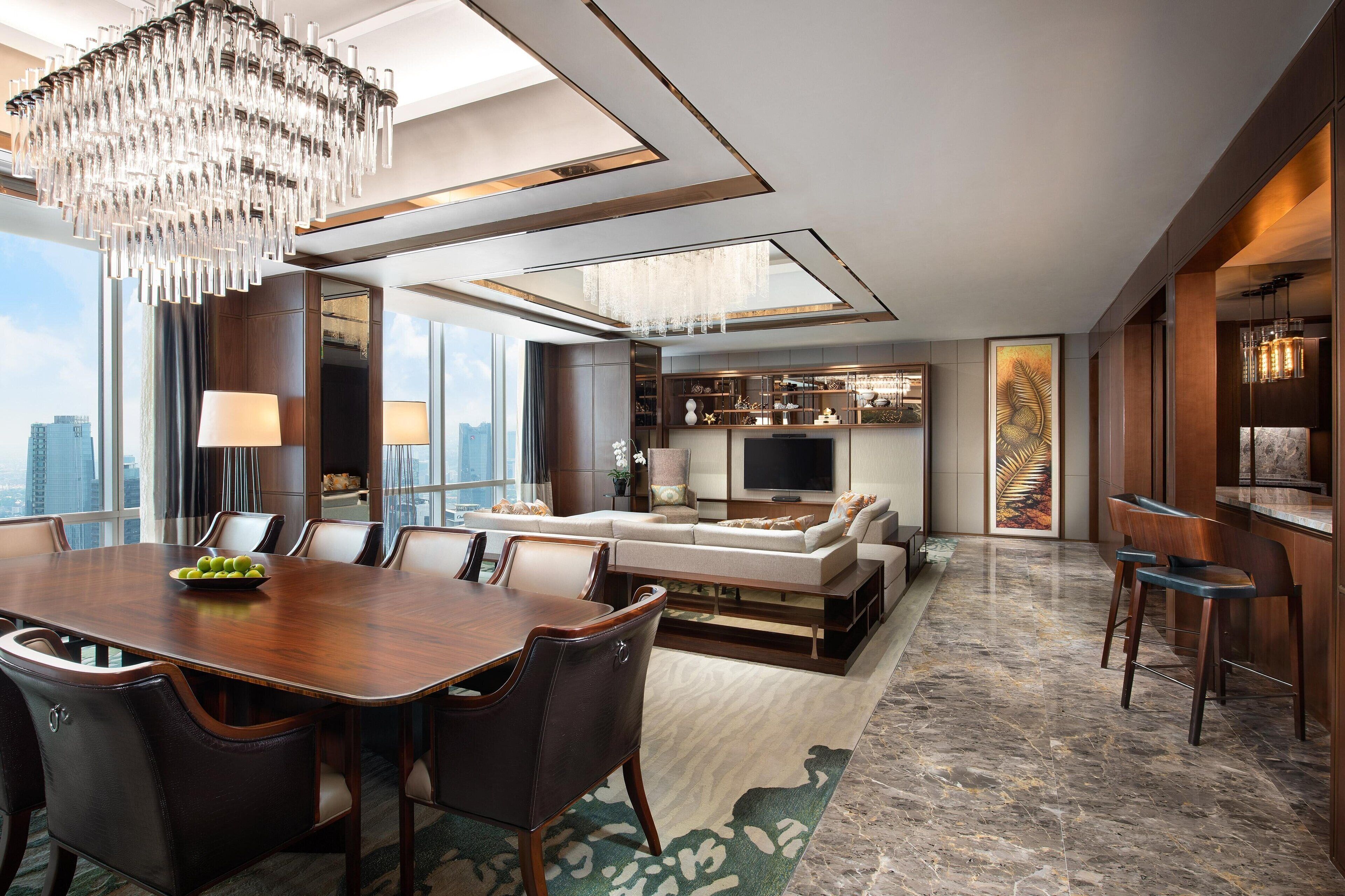 A modern hotel room with a dining area, a living room with a sofa and TV, and a bar area.