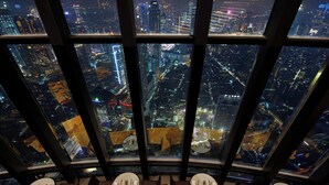 Un ristorante di lusso in un grattacielo, con vista panoramica sulla città, diversi tavoli e un design moderno.