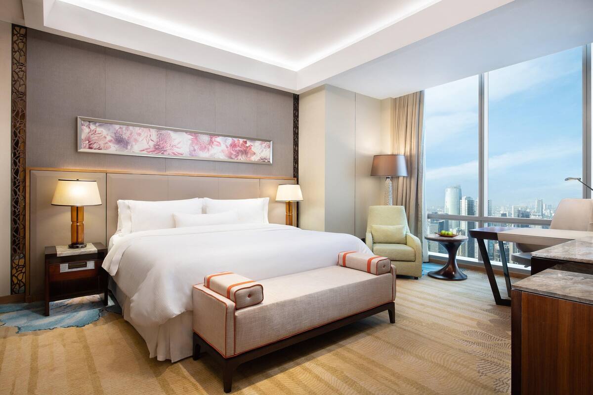 Hotelkamer met een groot bed, een bank, een bureau en een stoel. Groot raam met uitzicht over de stad.