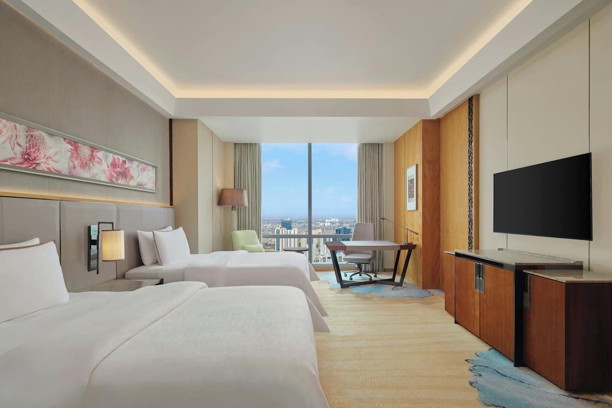 Hotelkamer met twee bedden, een bureau, een stoel, een televisie en een groot raam met uitzicht over de stad.