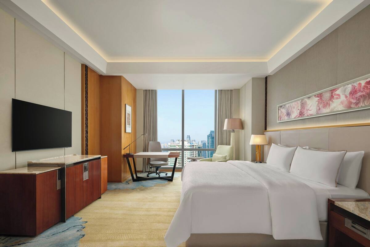 Een hotelkamer met een bed, bureau, stoel, televisie en uitzicht over de stad.