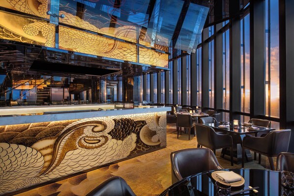 Un restaurante moderno con un diseño de escamas de pez en la barra, ventanas amplias y vistas panorámicas de la ciudad.