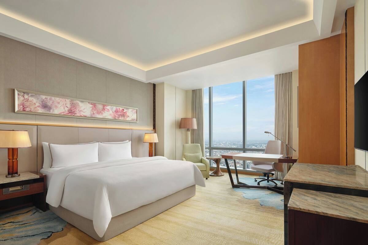 Hotelkamer met een groot bed, een bureau, een stoel, een televisie en een raam met uitzicht over de stad.