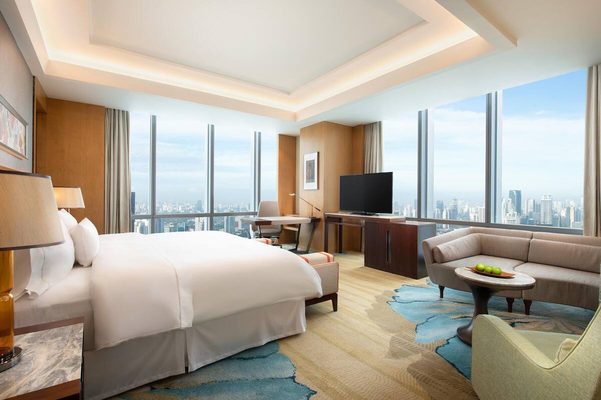 Hotelkamer met een groot bed, een bank, een bureau en een televisie. Groot raam met uitzicht op de stad.