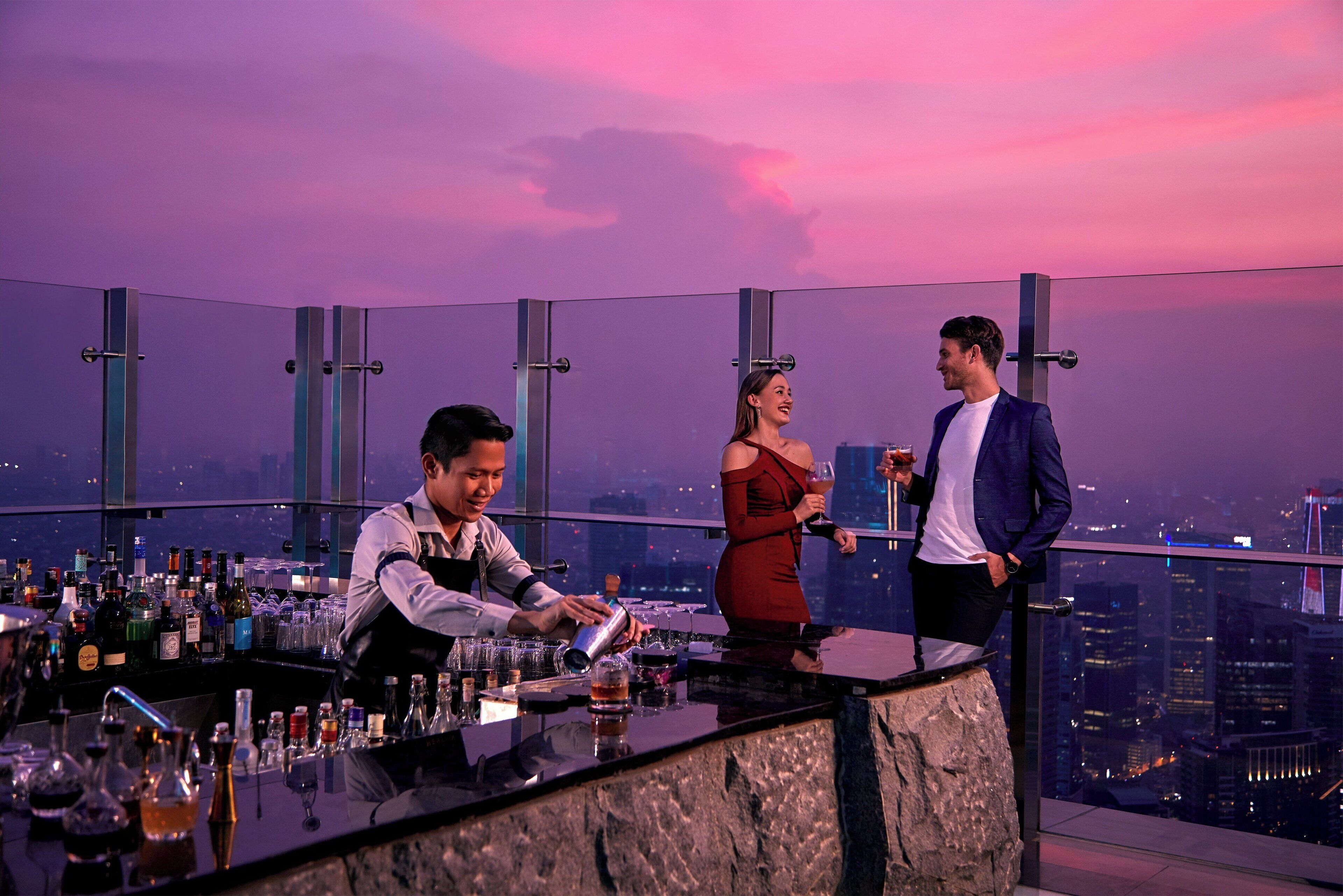Un bar con vistas a la ciudad, un camarero y dos clientes.