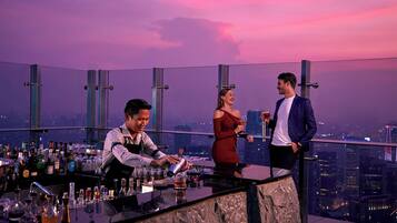Un bar con vistas a la ciudad, un camarero y dos clientes.