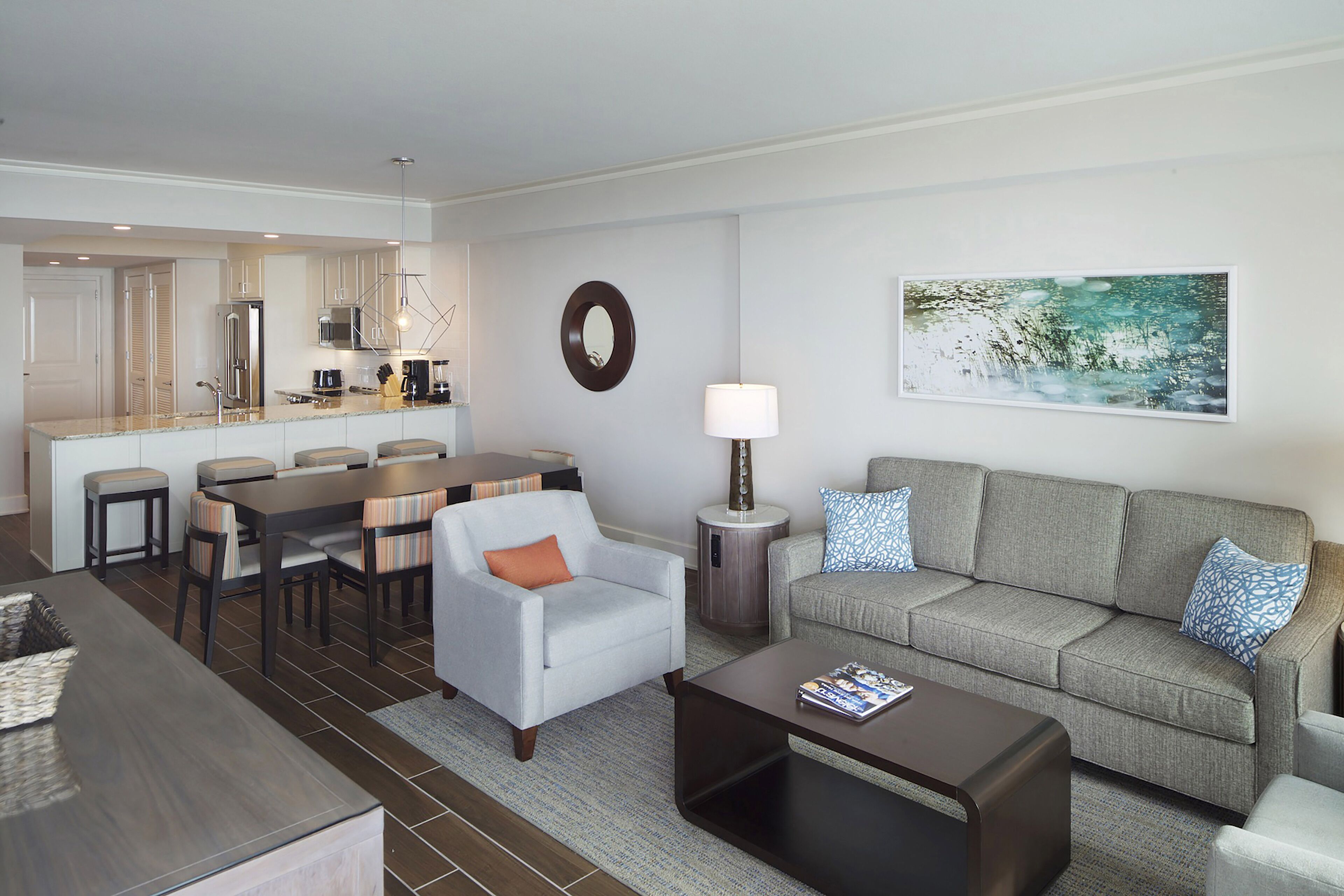 A modern living room with a grey sofa, a coffee table, a dining area with a table and chairs, and a kitchen in the background.