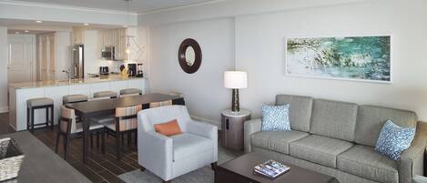 A modern living room with a grey sofa, a coffee table, a dining area with a table and chairs, and a kitchen in the background.