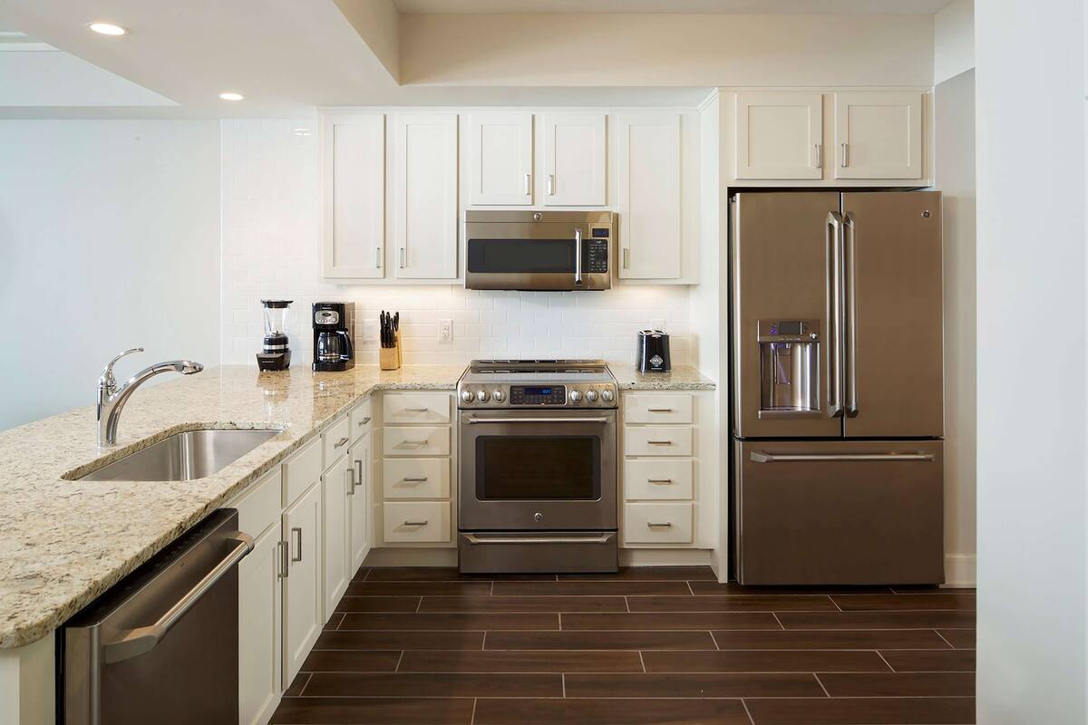 Una cocina moderna con armarios blancos, electrodomésticos de acero inoxidable y encimera de granito.