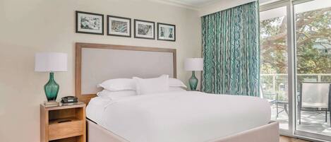 A modern hotel room with a large bed, two bedside tables, a ceiling fan, and a balcony with a view.