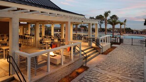 An outdoor dining area with tables and chairs, a pool, and palm trees.