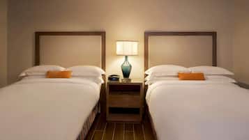 Une chambre d’hôtel avec deux lits, chacun agrémenté de draps blancs et d’un coussin décoratif orange. Une table de chevet avec une lampe se trouve entre les deux lits.