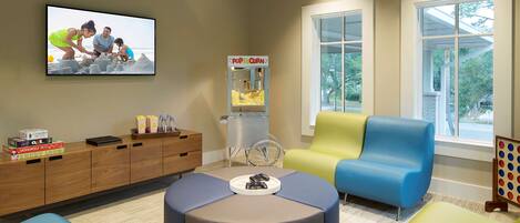 A modern living room with a TV, a popcorn machine, comfortable seating, and a bookshelf with board games.