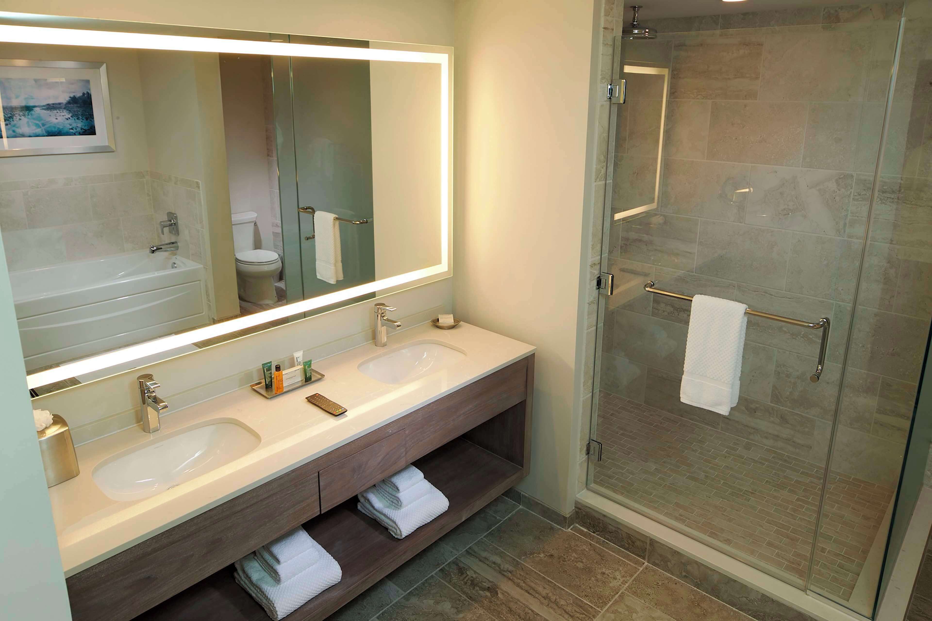 Un baño moderno con tocador doble lavamanos, un espejo grande y cabina de ducha con paredes de vidrio.